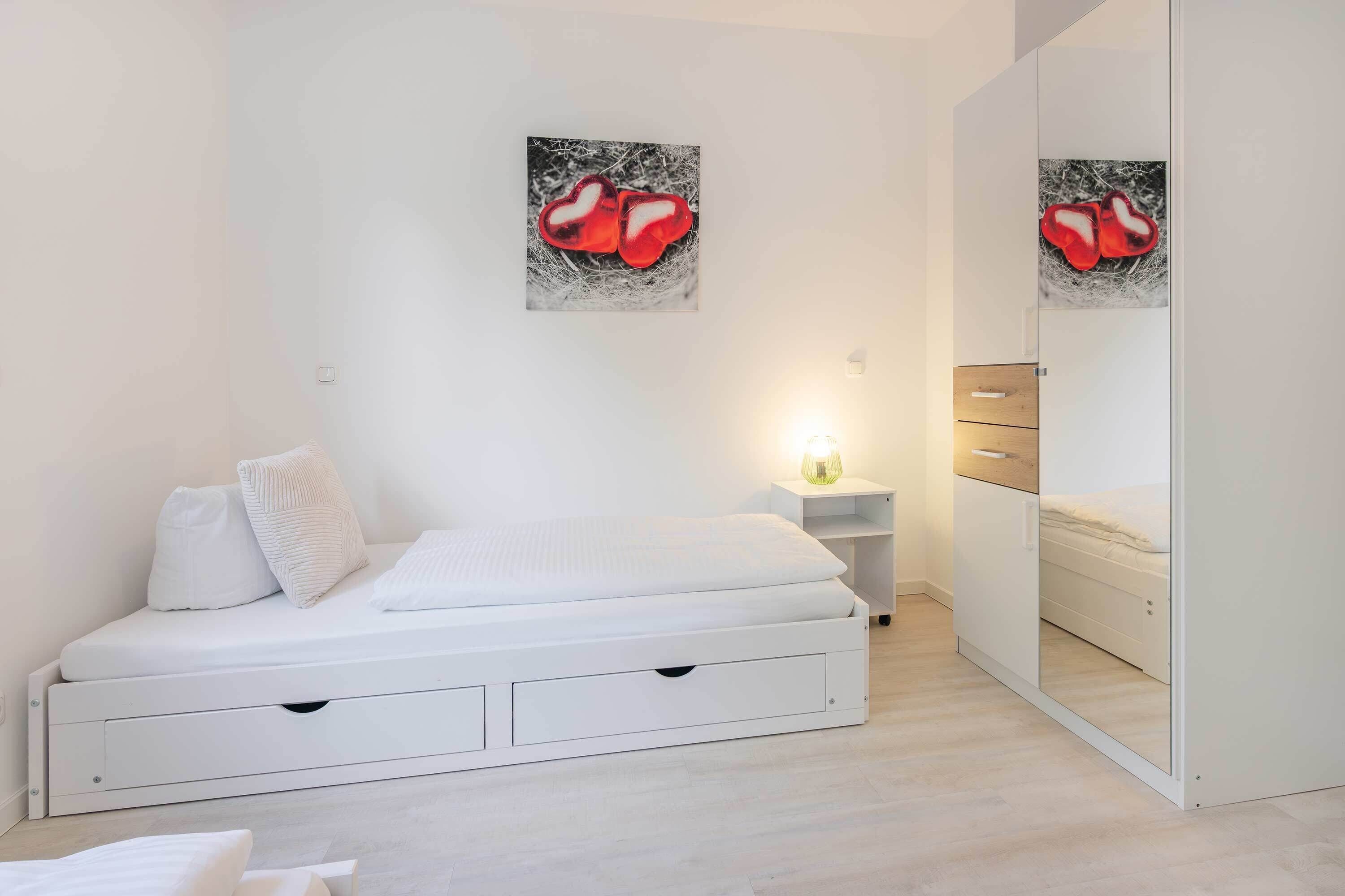 Una camera da letto moderna con un letto bianco, un comodino, uno specchio e un'opera d'arte appesa al muro.