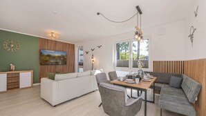 Ein moderner Wohnbereich mit Essplatz, einer Couch, einer Wand mit Holzverkleidung und einem großen Fenster.
