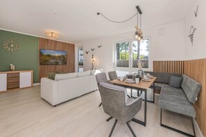 A modern living space with a dining area, a sofa, a wooden accent wall, and a large window.