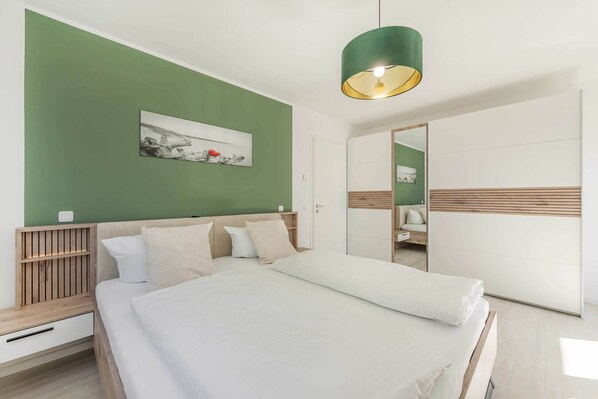 A modern bedroom with a bed, bedside tables, a hanging light fixture, a mirror, and a green accent wall.