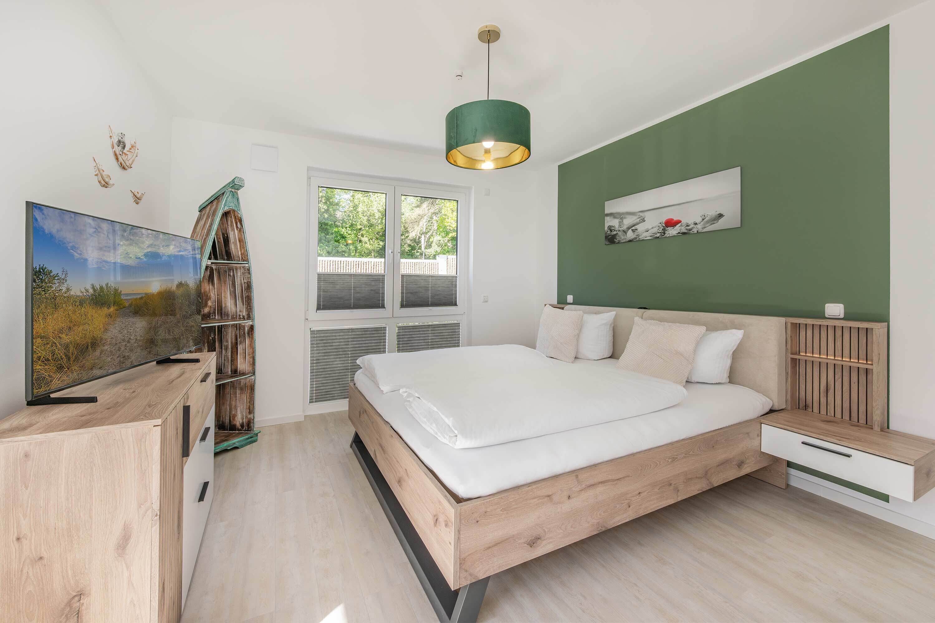 Une chambre à coucher avec un lit, une télévision, une armoire en bois, une fenêtre et un mur vert.