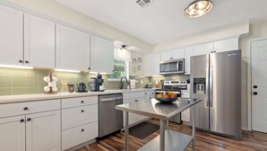 A modern kitchen with white cabinets, stainless steel appliances, and a wooden floor. - The Rover - Market District - 1m to DT Bentonville (Bentonville)