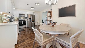A modern kitchen with white cabinetry, stainless steel appliances, and a dining area with wicker chairs and a round table. - The Rover - Market District - 1m to DT Bentonville (Bentonville)