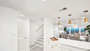 Une cuisine moderne avec des meubles blancs, un plan de travail en bois et des luminaires suspendus.