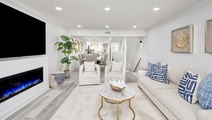 Un salon moderne avec une cheminée, un téléviseur à écran plat, un coin repas et une cuisine en arrière-plan.