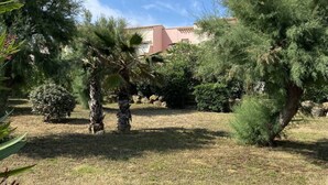 A garden with various trees and shrubs, a building with a red roof in the background, and a clear blue sky. - APPARTEMENT VILLA 7PERSONNES LE CAP D'AGDE Résidence PORT LANO Plage LA ROQUILLE (Agde)