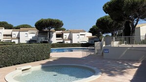 A swimming pool area with a circular pool, surrounded by a paved walkway, and adjacent to a row of buildings with a tiled roof. - APPARTEMENT VILLA 7PERSONNES LE CAP D'AGDE Résidence PORT LANO Plage LA ROQUILLE (Agde)