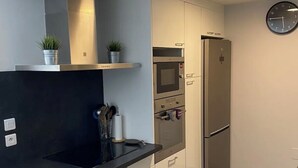 A modern kitchen with a black countertop, stainless steel appliances, and a clock on the wall. - APPARTEMENT VILLA 7PERSONNES LE CAP D'AGDE Résidence PORT LANO Plage LA ROQUILLE (Agde)