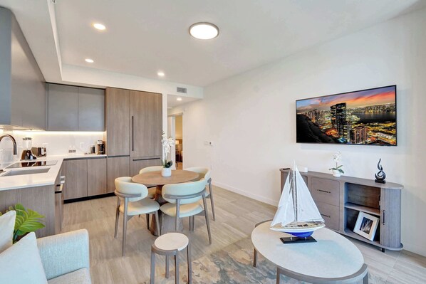 Una cocina moderna con electrodomésticos integrados, un comedor con una mesa redonda y sillas, y un cuadro de un paisaje urbano en la pared.