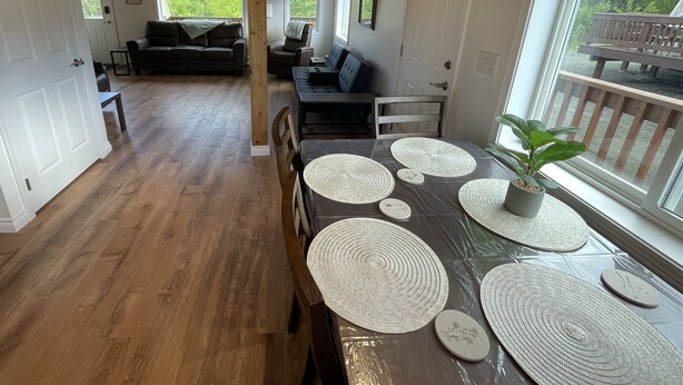 Un vaste espace dédié à la salle à manger, avec une table en bois et des sets de table en fibres tressées, un banc en bois et une vue sur l’extérieur grâce à de grandes fenêtres.
