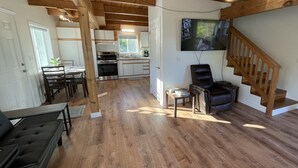 Un vaste espace de vie doté d’un plancher en bois, d’une table à manger avec des chaises, d’un fauteuil en cuir noir et d’un escalier avec des rampes en bois.