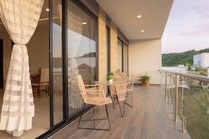 A balcony with wicker furniture, a glass door, and a view of a hotel building. - EOS Suites (Santa Maria Huatulco)