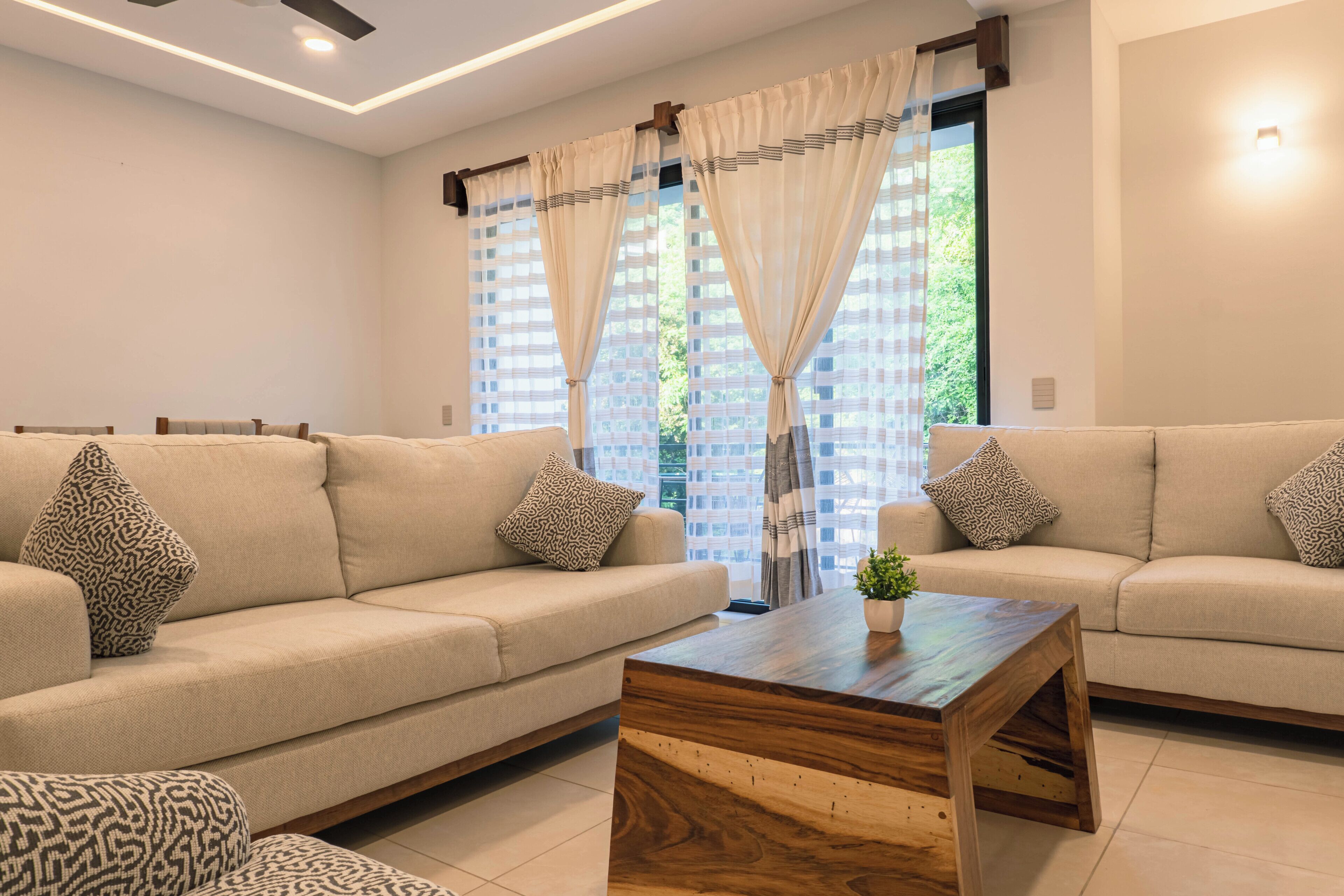 Ein modernes Wohnzimmer mit zwei Sofas, einem Holztisch und Blick durch große Fenster.