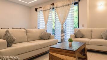 Ein modernes Wohnzimmer mit zwei Sofas, einem Holztisch und Blick durch große Fenster.