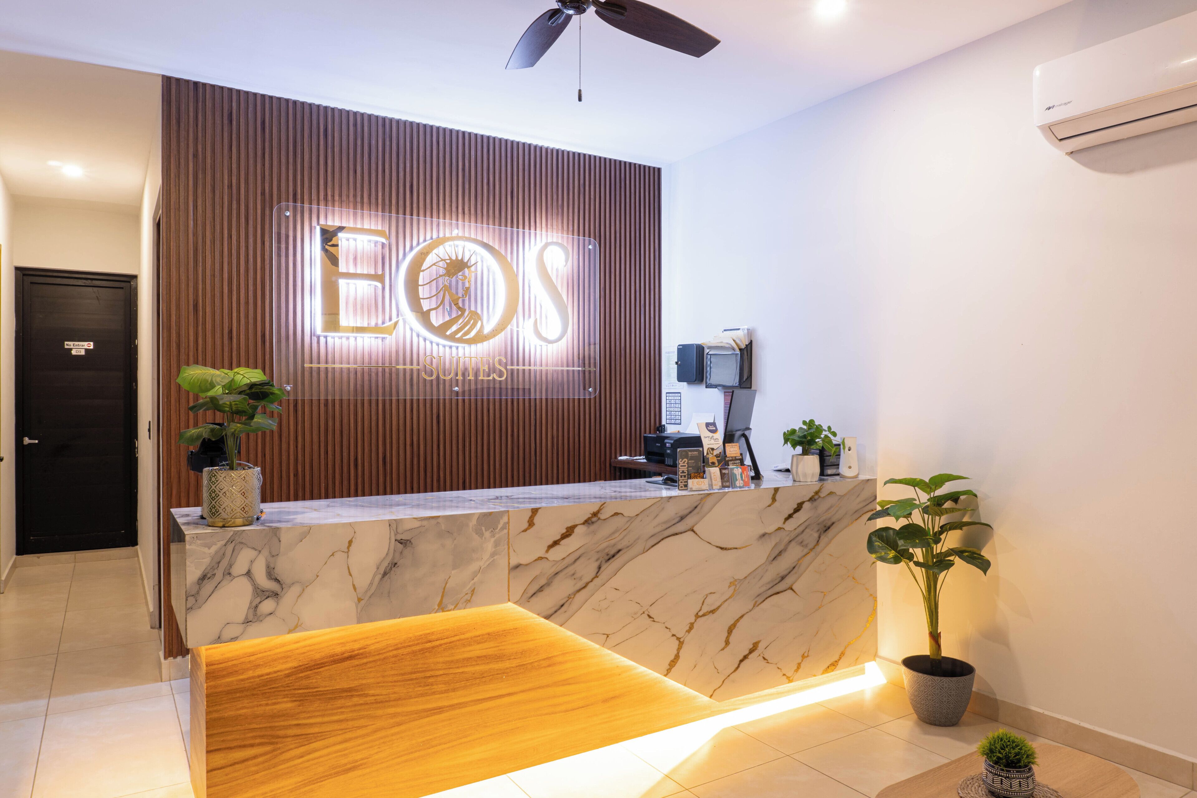 A hotel reception desk with a wooden panel backdrop, a marble counter, and a ceiling fan.