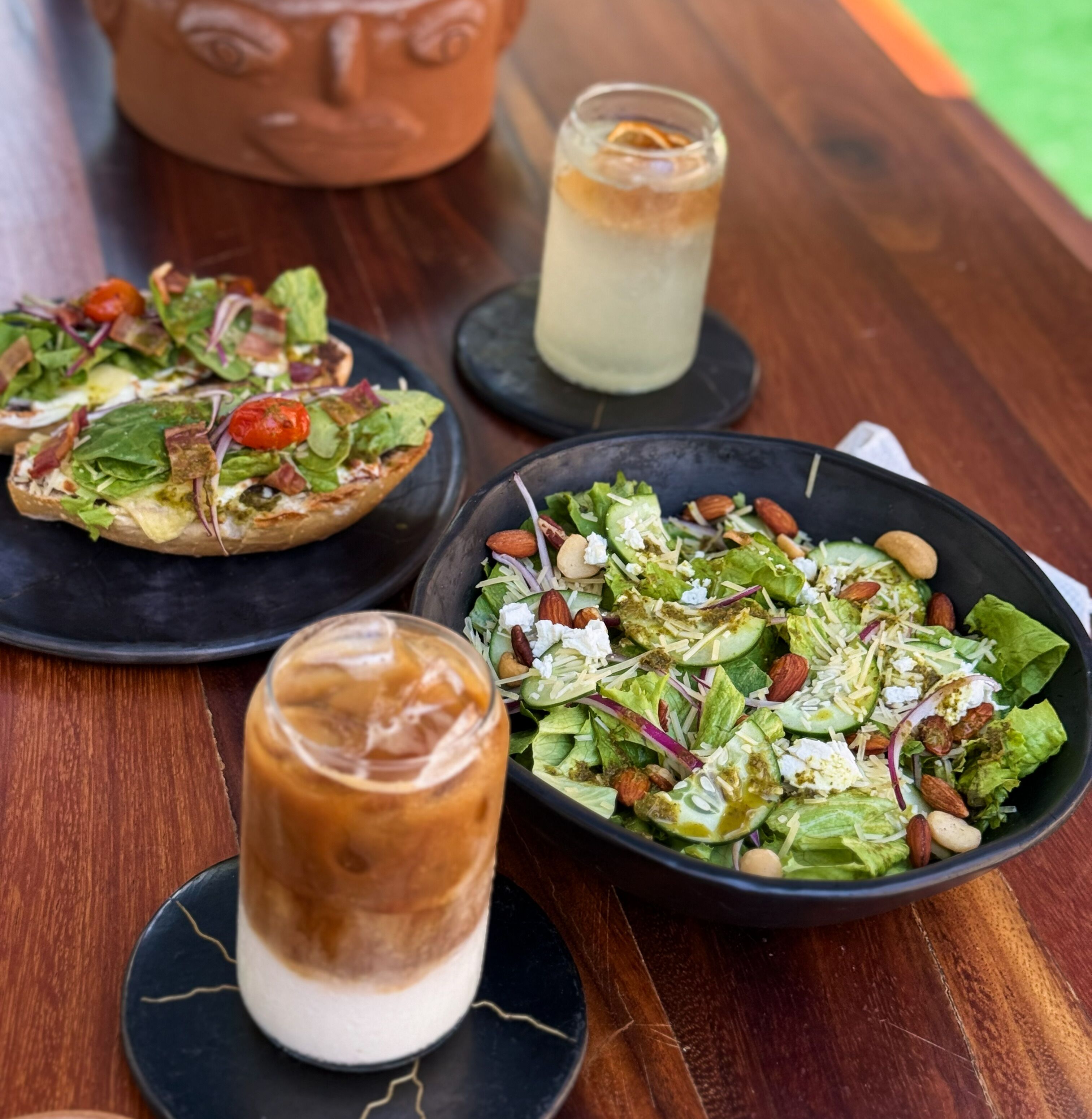 A wooden table with a salad, a glass of iced drink, and a pizza.