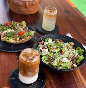 Une table en bois avec une salade, un verre de boisson fraîche et une pizza.