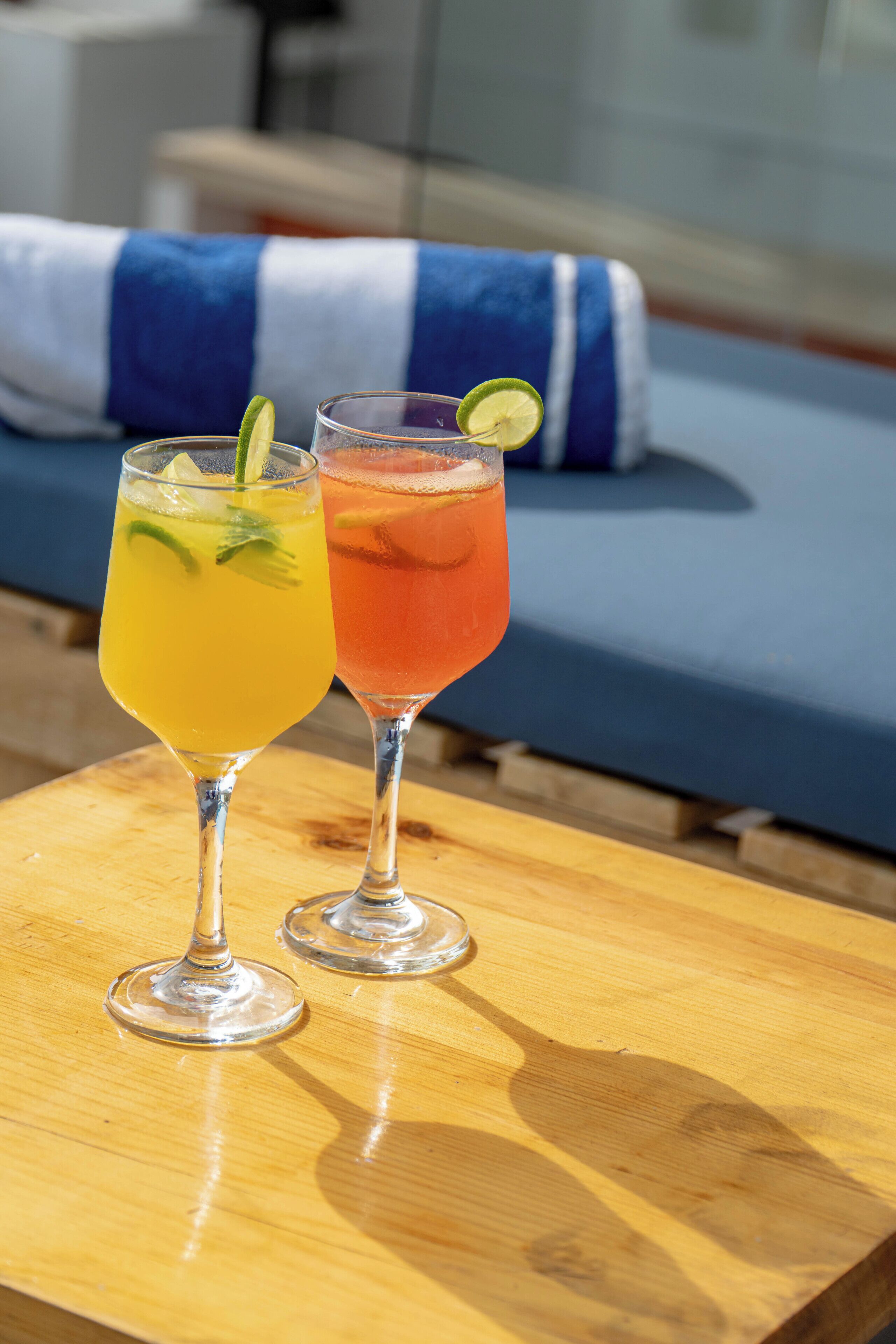 Two cocktails on a wooden table with a blue and white striped cushion in the background.