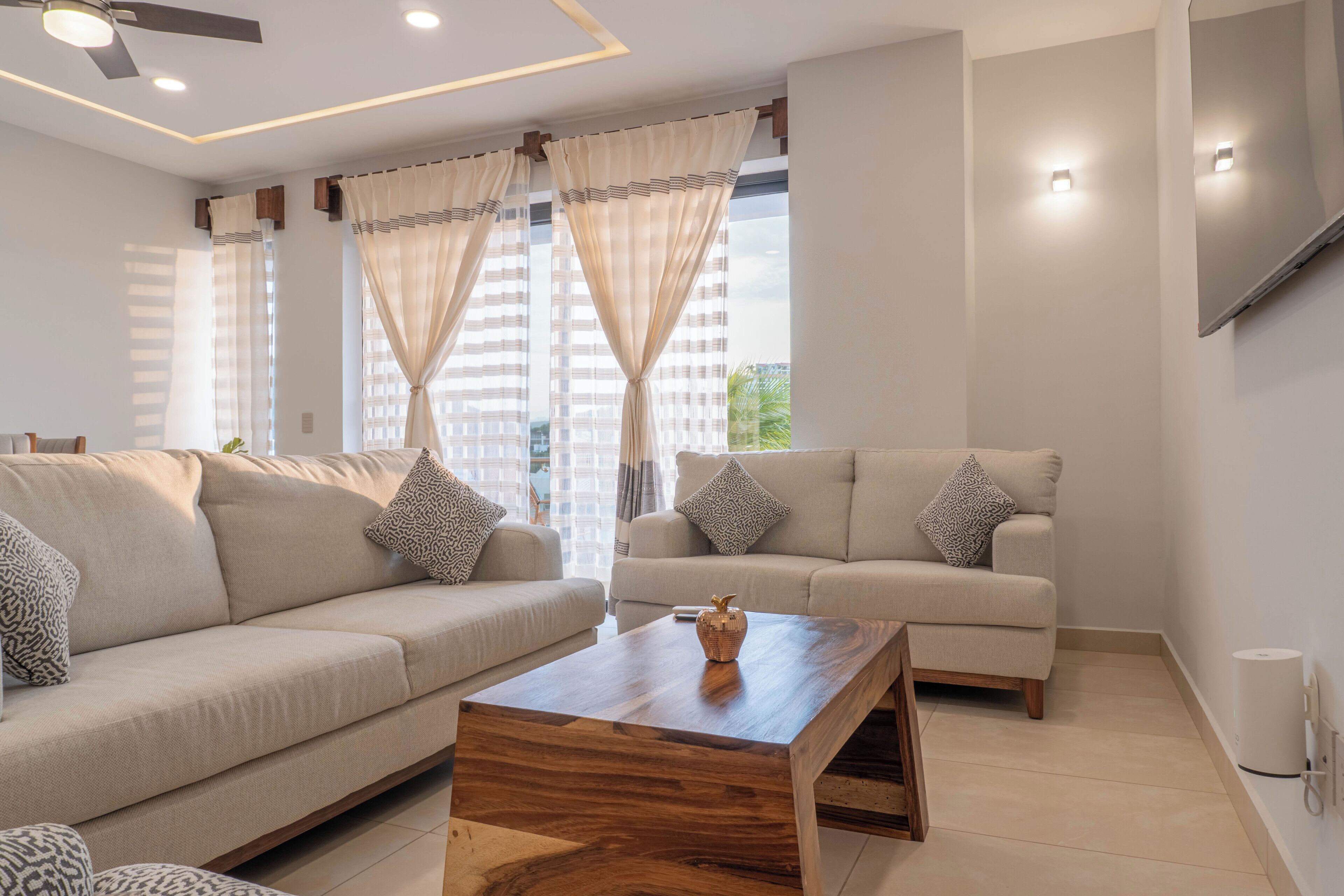 A modern living room with two sofas, a wooden coffee table, and a ceiling fan.