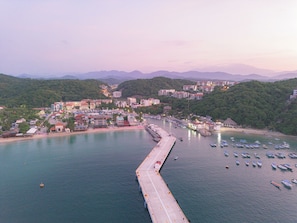 A coastal town with a pier extending into the water, surrounded by buildings and greenery. - EOS Suites (Santa Maria Huatulco)