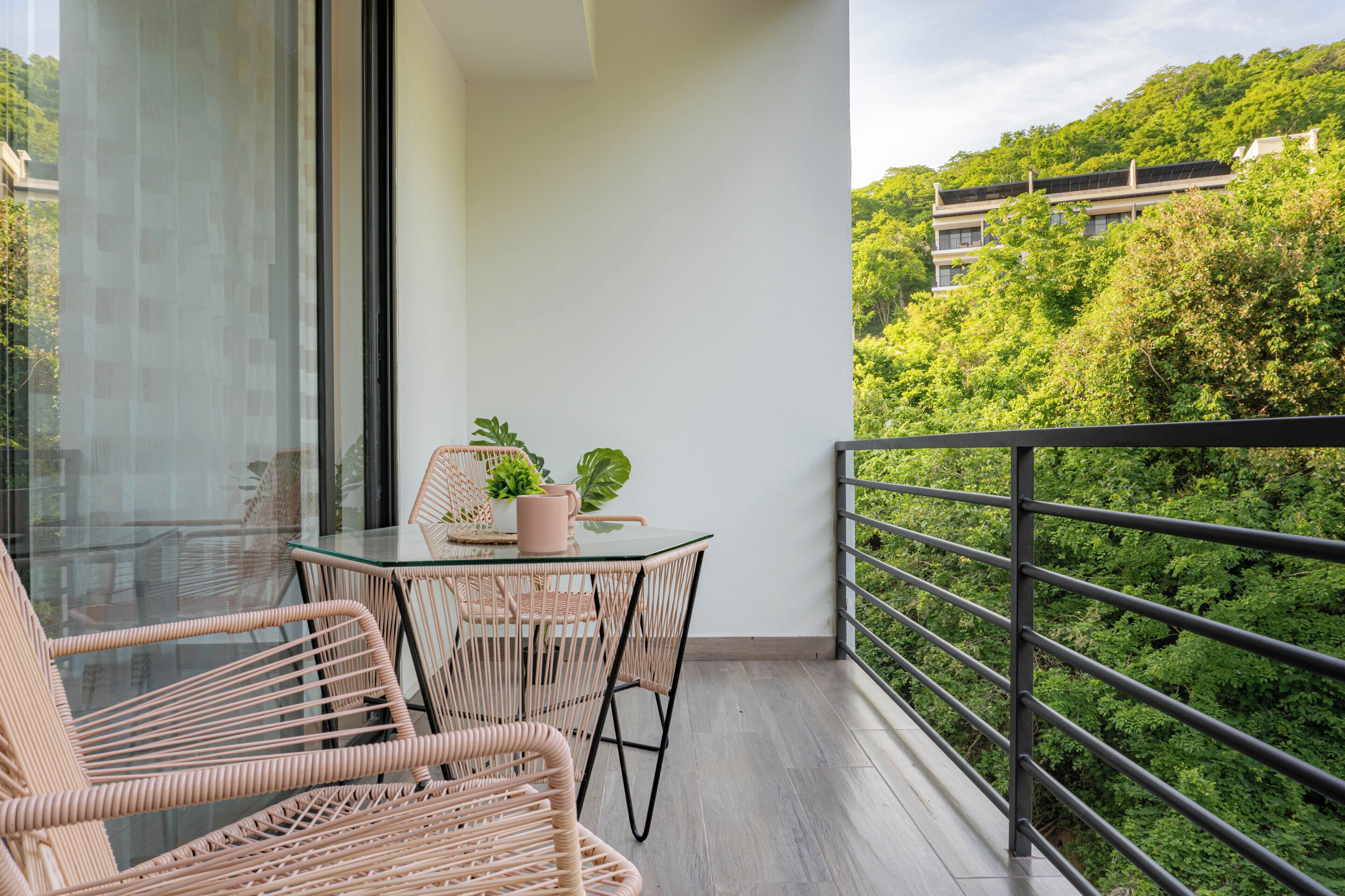 A balcony with wicker furniture, a glass table, and a potted plant.