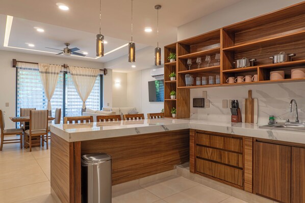 A modern kitchen with wooden cabinets, a marble countertop, and a dining area with a table and chairs.
