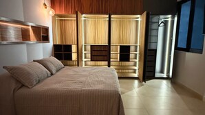 A bedroom with a bed, a wardrobe with multiple compartments, and a door leading to another room. - EOS Suites (Santa Maria Huatulco)