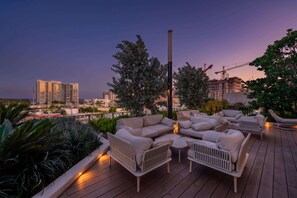 A rooftop terrace with outdoor seating, a view of the city skyline, and a construction crane in the background.