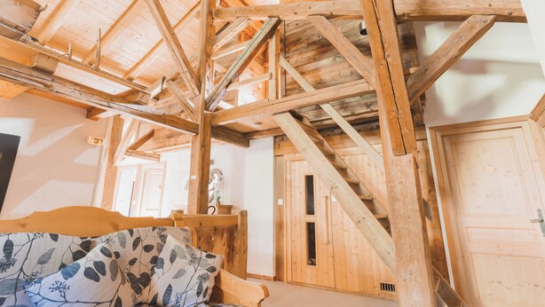 A wooden interior with exposed beams, a bed with patterned bedding, and a door leading to another room.