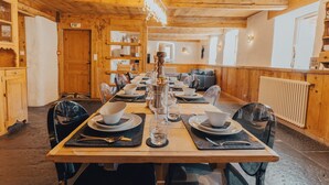 A long wooden dining table set with plates, bowls, and glasses, flanked by chairs.