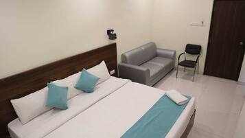 Una habitación de hotel con una cama, un sofá gris, una pequeña silla y un cabecero de madera.