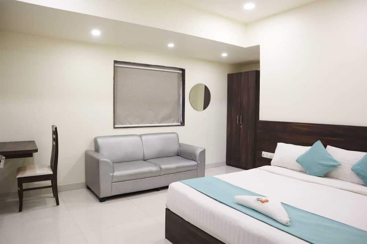 A bedroom with a bed, a grey sofa, a desk, and a wardrobe.