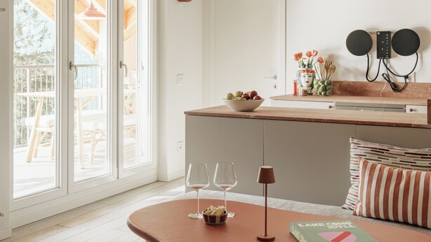 Una cocina moderna con techo de madera, un comedor con mesa redonda y vistas a una terraza exterior a través de amplios ventanales.