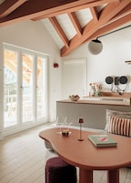 Una cocina moderna con techo de madera, un comedor con mesa redonda y vistas a una terraza exterior a través de amplios ventanales.