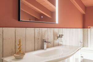 Un baño con un lavamanos blanco, un cuenco decorativo dorado, un espejo y un panel de pared de madera.