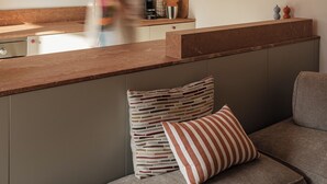 Una cocina moderna con encimera de madera, horno empotrado y un perchero. Hay una zona de estar con un banco acolchado y un cojín.