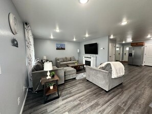 A modern living room with grey sofas, a flat-screen TV, and a fireplace.