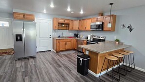 A modern kitchen with wooden cabinets, stainless steel appliances, a granite countertop, and a small island with stools.