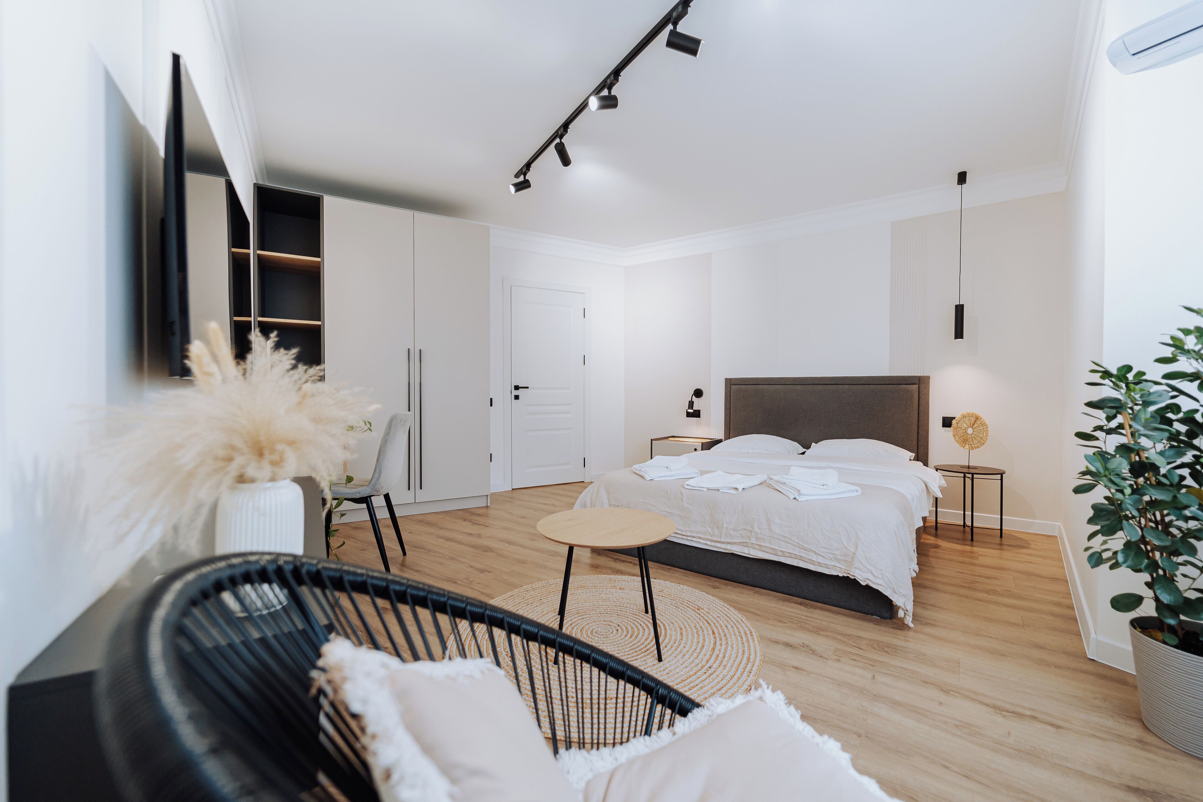 Une chambre à coucher moderne avec un lit, des tables de chevet, une chaise, une petite table et une plante en pot.