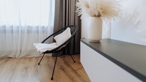 Ein modernes Zimmer mit einem schwarzen Drahtstuhl, einem weißen Kissen, einer Vase mit Pampasgras und Holzboden.