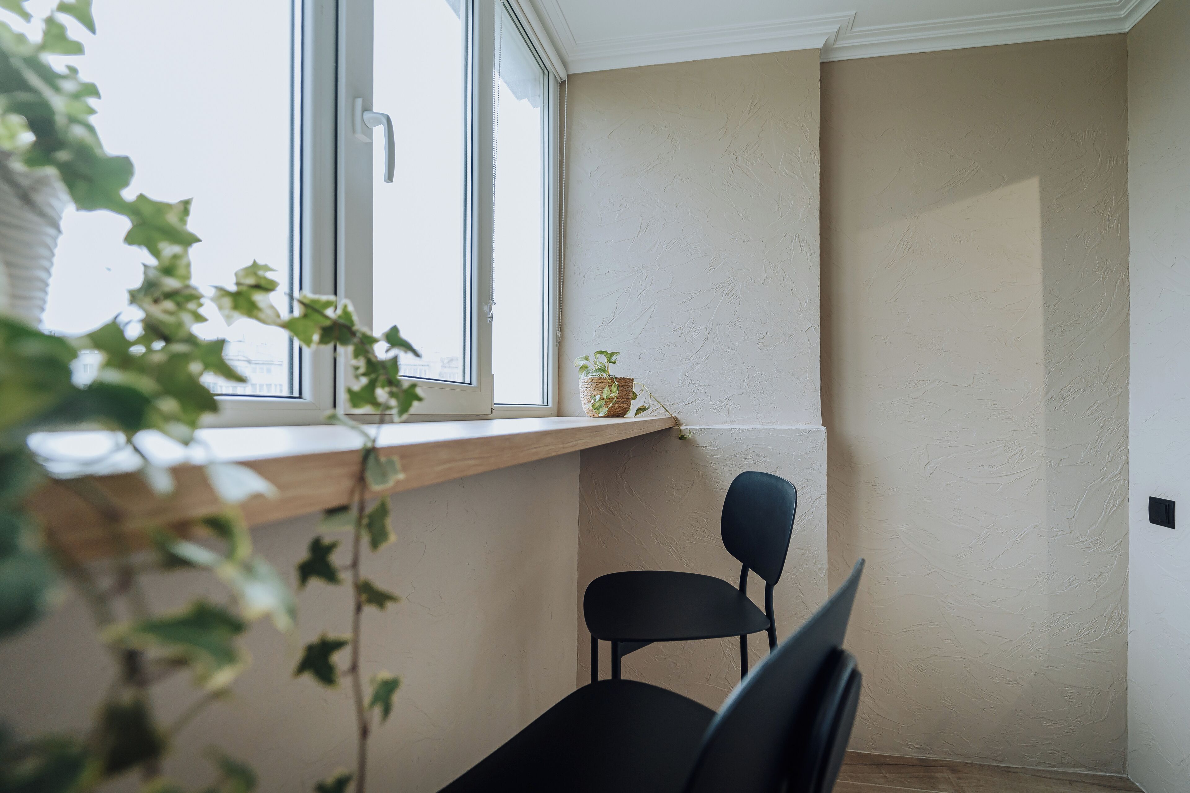 Et hjørneværelse med et vindue, en sort stol og en reol med en plante.