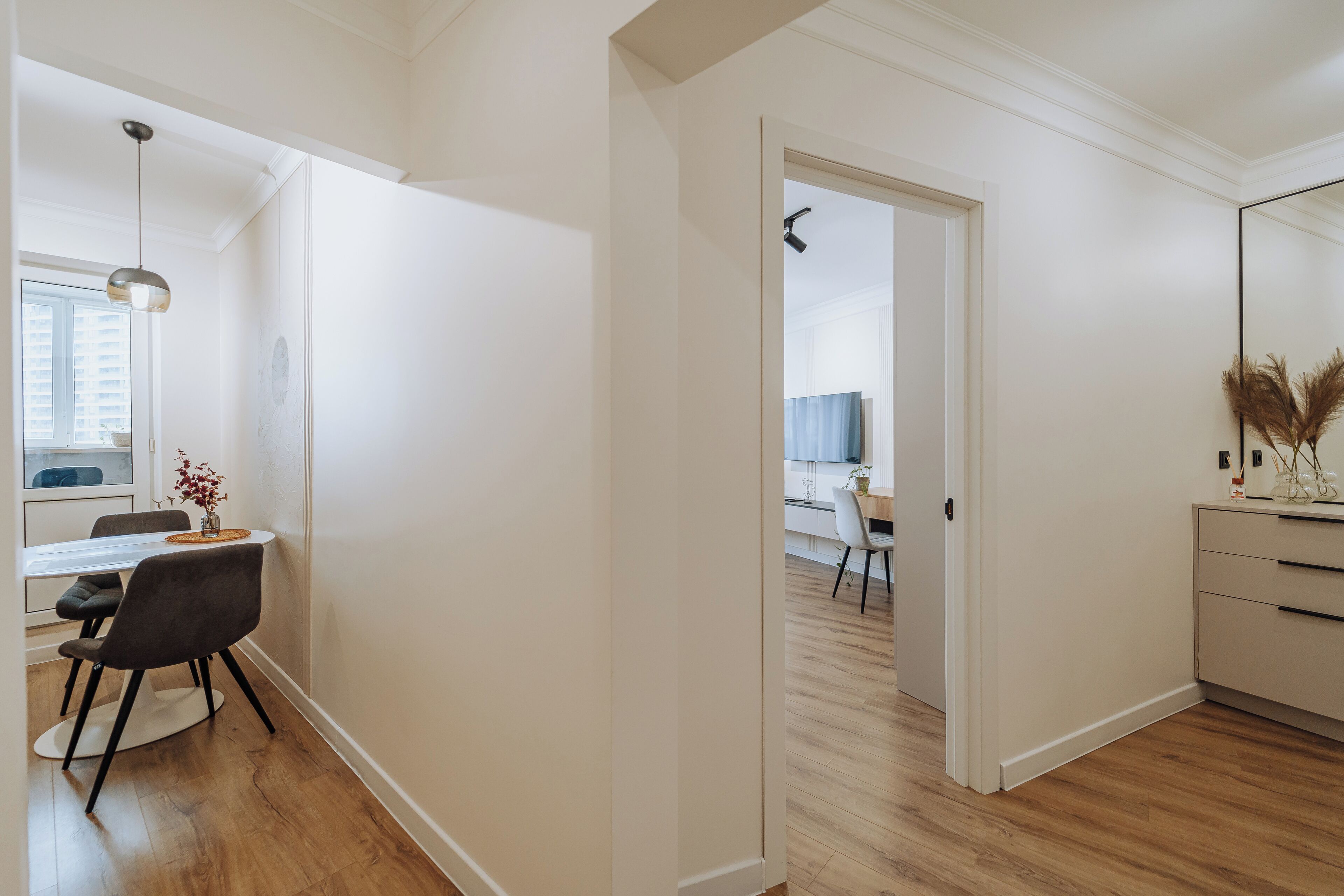 Une cuisine moderne avec des meubles blancs, un coin repas doté d’une table et de chaises blanches, et un couloir menant à une autre pièce.