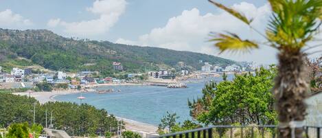 A coastal town with buildings along the shore, a beach, and a hilly backdrop.