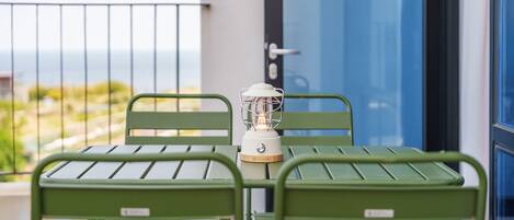 Un balcón con una mesa, dos sillas, un farol y vista al mar.