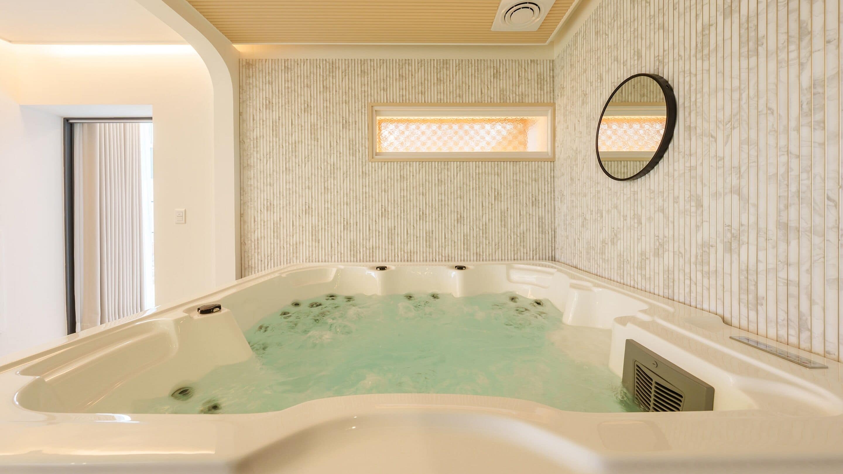 Ein Wellnessraum mit Whirlpool, Fenster und einem wandmontierten Spiegel.