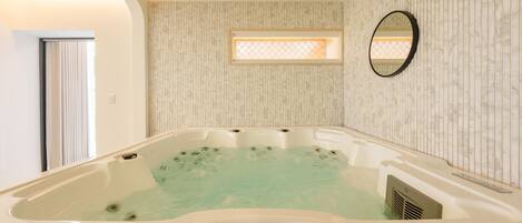 Ein Wellnessraum mit Whirlpool, Fenster und einem wandmontierten Spiegel.