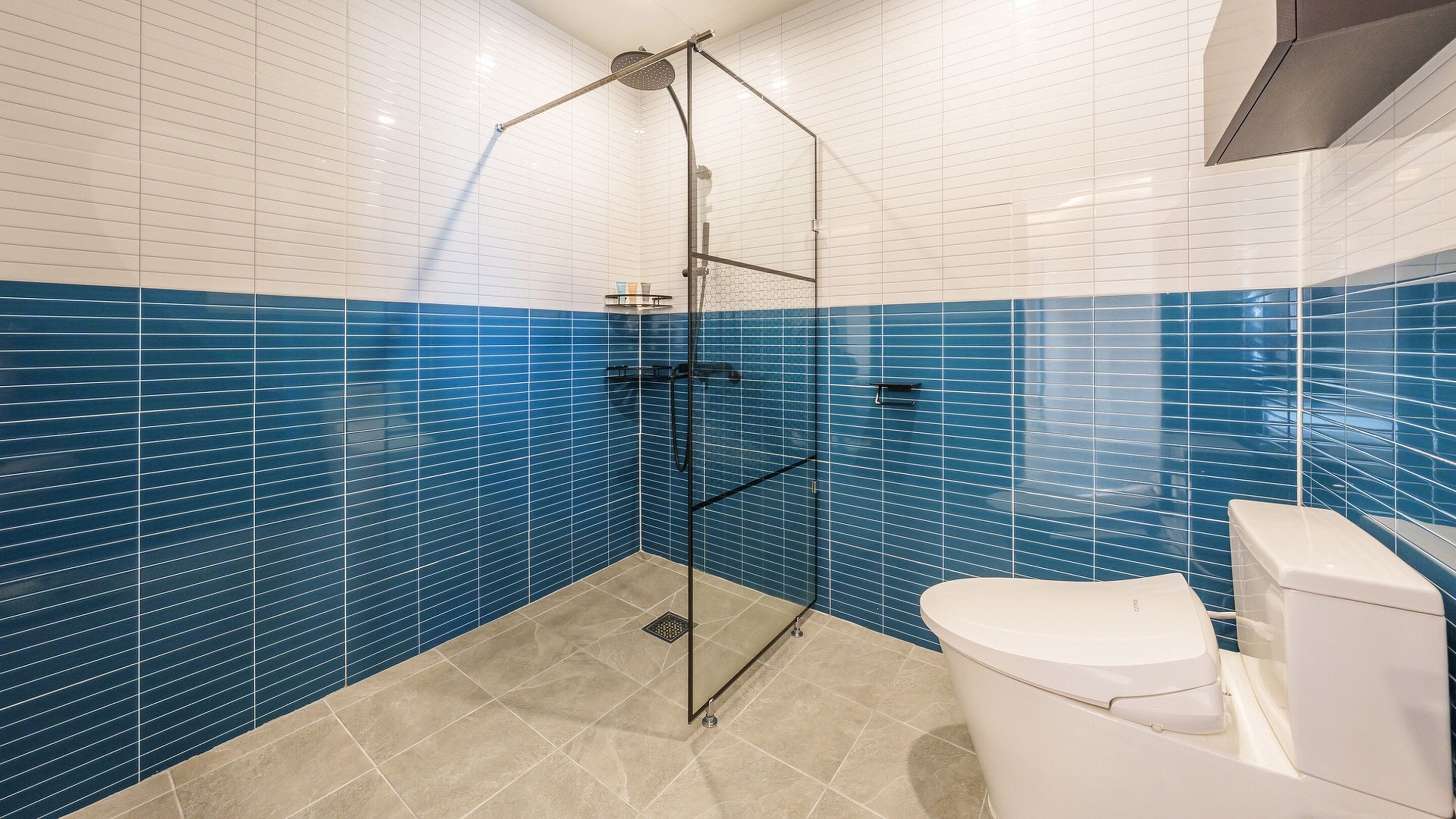 A bathroom with a glass-enclosed shower, white and blue tiled walls, and a white toilet.
