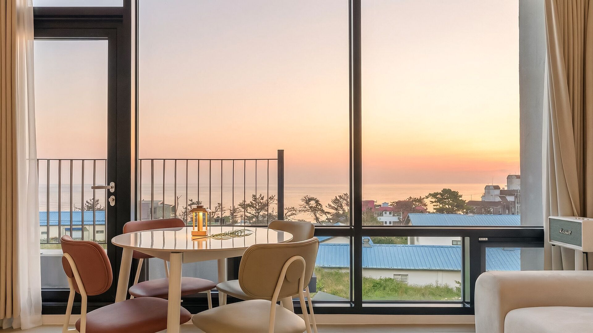 A balcony with a table and chairs, a view of the sea, and a cityscape in the background.