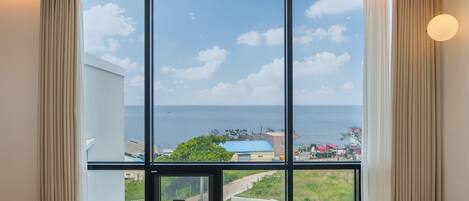 A room with a large window offering a view of the sea and a coastal town.