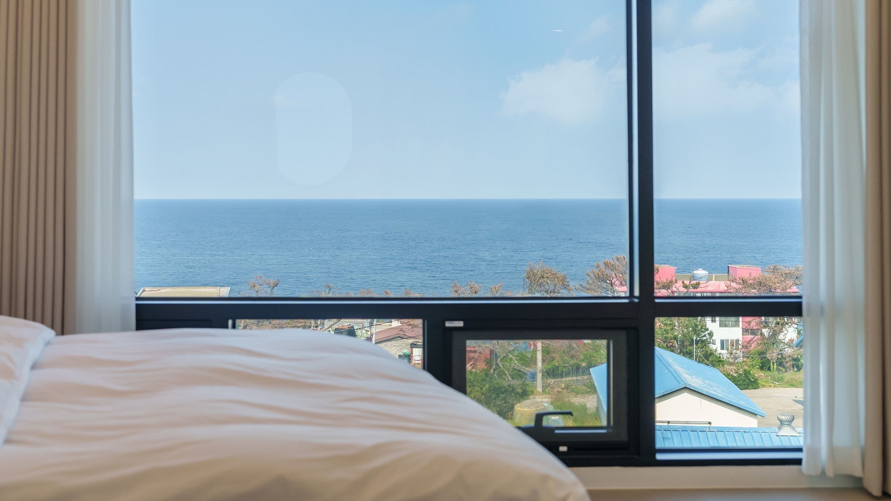 Quarto de hotel com uma janela grande que oferece vista para o mar e uma cidade costeira.
